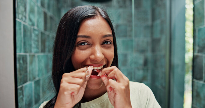 Dental floss, portrait and smile of woman in bathroom of home for getting ready or morning routine. Mouth, oral hygiene and mirror with happy Indian person in apartment for daily teeth cleaning