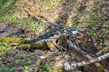 Discarded cable coils litter a verdant ravine, symbolizing environmental neglect and the remnants of scrap metal scavenging, amidst fresh spring foliage and a small creek