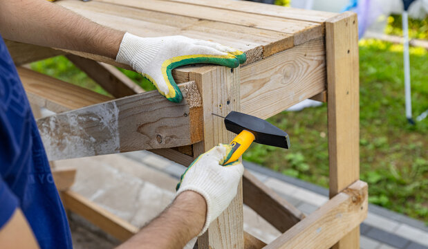 Close-up. Carpenter with hammer and nails fixes a wooden board. Construction industry, do it yourself. Wooden work table.