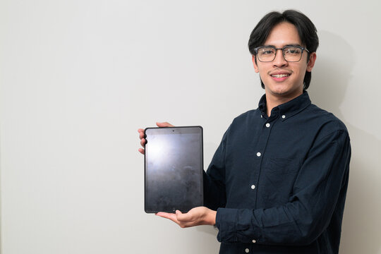 Portrait of handsome young Asian Thai man wearing eyeglasses using digital tablet computer - Powered by Adobe