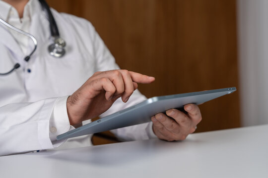 Close-up of doctor using digital tablet while wearing stethoscope and white coat, modern healthcare and technology concept in clinical setting.