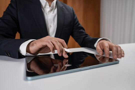 Businessman touching tablet screen with stylus in modern office environment, focused on hands and device interaction concept. - Powered by Adobe
