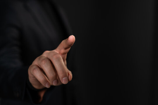 Businessman pointing with index finger in a gesture of touch on dark background, representing digital interaction or decision-making concept.