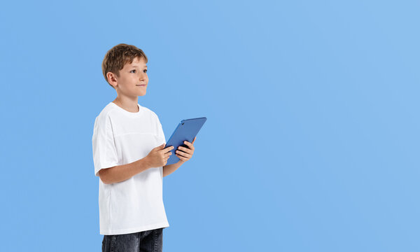 Young boy holding tablet while looking away, wearing white shirt