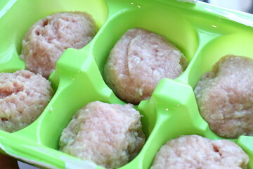 A green plastic container filled with meatballs