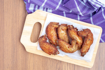 A top-down view of six fried chicken wings, a protein-rich food, served on white paper on a wooden cutting board with a purple napkin.