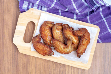 A top-down view of six fried chicken wings, a protein-rich food, served on white paper on a wooden cutting board with a purple napkin.