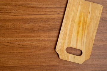 A top-down view of a light wooden cutting board, with a handle cutout, resting on a background of darker wooden planks. Significant copy space is on the left.