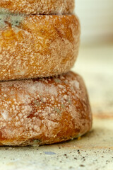 A vertical close-up of two stacked, round bread loaves. The crusts are covered in blue-green Penicillium mold and white spots, indicating food spoilage.