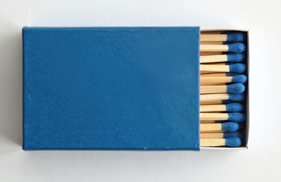 A blue matchbox lies open showing multiple wooden matches with blue tips. These essential items are isolated on a clean white surface, ready for use.