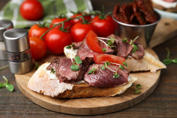 Delicious bruschettas with roast beef served on wooden table, closeup