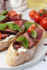 Delicious bruschettas with roast beef served on white table, closeup