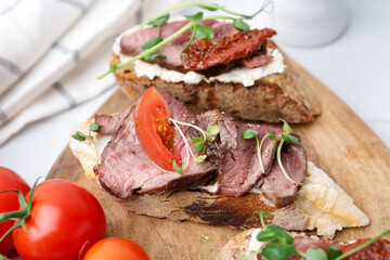 Delicious bruschettas with roast beef served on white table, closeup