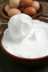Whipped egg whites in bowl, whisk and ingredients on table, closeup