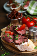 Delicious bruschettas with roast beef served on wooden table, closeup