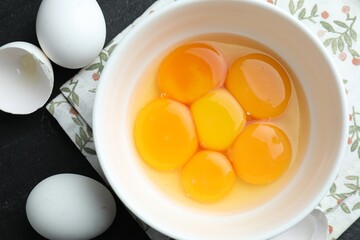Raw eggs and yolks on black table, flat lay