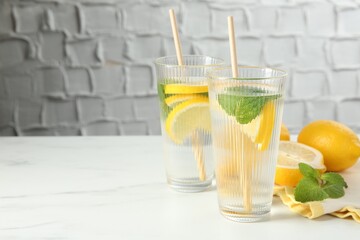 Refreshing water with lemons and mint on white marble table, closeup. Space for text