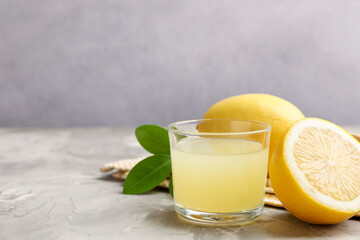 Lemon juice in glass, leaves and fresh lemons on light grey table, closeup. Space for text