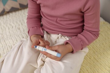 Diabetes. Little girl checking blood sugar level with lancet pen on bed, closeup