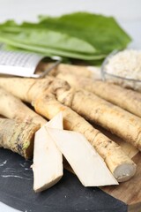 Whole and grated horseradish roots, grater and green leaves on table, closeup