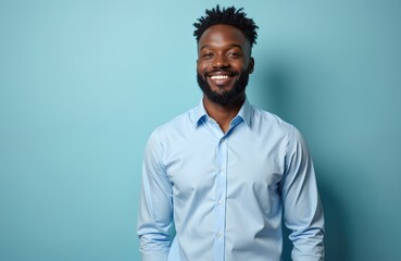 Obraz premium Young african american man smiles confidently in studio portrait. Wears light blue shirt, presents positive expression. Background solid blue creating clean, modern feel. Image represents success,