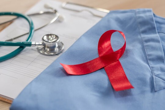 World aids day and national HIV AIDS and ageing awareness month concept with red ribbon on medical or surgical doctor's lab uniform on work desk in hospital background