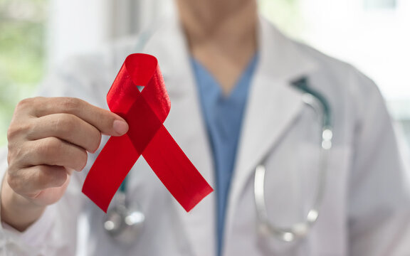 World aids day and national HIV AIDS and ageing awareness month with red ribbon on medical or surgical doctor's hand in hospital background