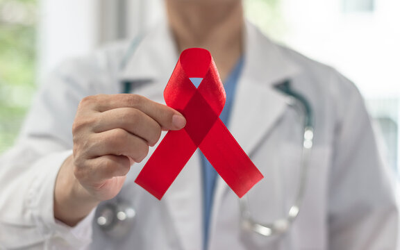 World aids day and national HIV AIDS and ageing awareness month with red ribbon on medical or surgical doctor's hand in hospital background