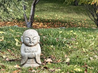Stone Buddha statue surrounded by autumn leaves in garden  