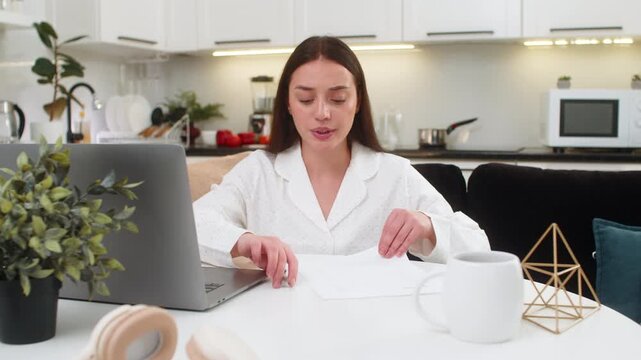 Young woman at home crumples wrong bill throws page beside laptop plans to print new fixed copy. Caucasian girl on sofa sits at table looks upset prepares fresh invoice checks amount types again calm.