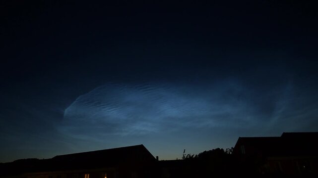 Noctilucent clouds glowing over quiet suburban rooftops