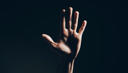 Male hand raised forward in stop gesture under harsh light on dark background, symbol of warning, caution, and awareness.