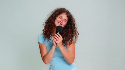 Young woman enthusiastically singing into microphone performing expressively joyful mood showcasing vocal talent. Girl on gray background happily enjoying musical experience cheerful energetic emotion - Powered by Adobe