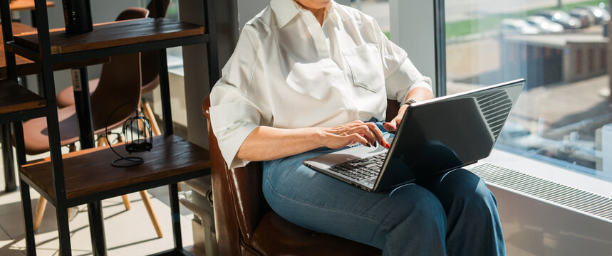 Woman typing on laptop near window in bright cafe interior. Banner with copy space and empty place for advertising. Focus, creativity, and productive work atmosphere in modern lifestyle. - Powered by Adobe