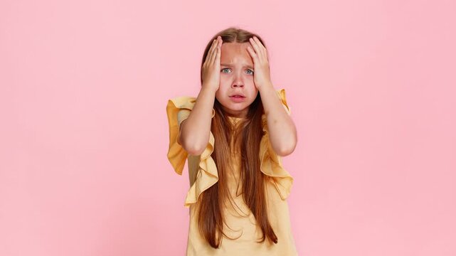 Young child girl covers mouth with hands stares with wide open eyes, expressing fear, panic surprise in emotional way, reacting to imaginary danger or unexpected sound. School kid on pink background.
