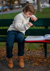Portrait of a 7-year-old boy drawing in the park on an autumn day