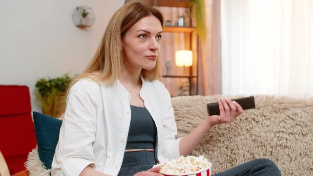Middle-aged woman enjoys watching comedy show on TV at home, laughing openly with cheerful face. Young adult girl feels amused and carefree, connecting emotionally with lighthearted entertainment.