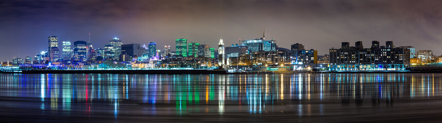 Wide panorama of downtown Montreal in winter. Long exposure night shot with the city lights reflected in the St Lawrence river.