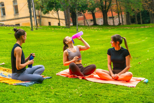 Women friends relaxing in park drinking water after yoga