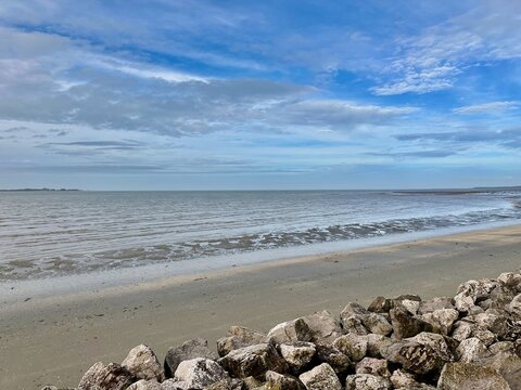 Peaceful beach and seawall of Le Crotoy in the Somme Bay, France, with calm waves, cloudy sky, and rocky shoreline at low tide creating a serene coastal landscape and tranquil seaside atmosphere