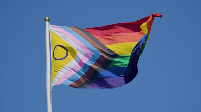 Colorful inclusive pride flag waving under blue sky