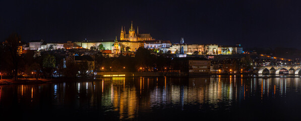 Wide, night panorama of the Royal Castle in Prague and its reflection in the river. 