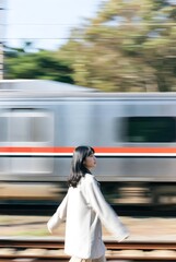 A young Asian woman walks beside a high-speed train in an industrial setting, in a moody cinematic style.