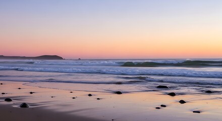 Obraz premium Gentle ocean waves under a soft, pastel sunset sky at a rocky beach