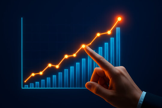Business hand pointing to the highest point on a glowing orange line graph overlaid on a rising blue bar chart symbolizing successful peak performance financial investment achievement and market goals