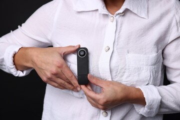 Young woman with hidden spy camera in her pocket on black background, closeup