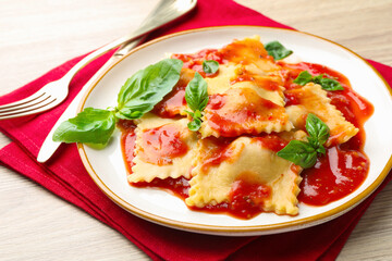 Delicious ravioli with tomato sauce and basil served on light wooden table, closeup