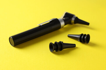 Hearing test. Modern otoscope and ear speculums on yellow background, closeup