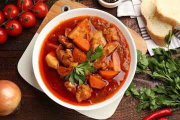 Delicious cooked stew with fresh ingredients and bread on wooden table, flat lay