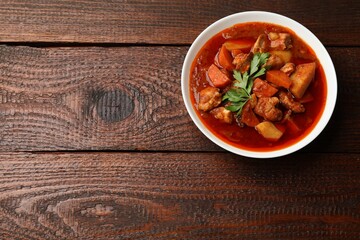 Delicious cooked stew in bowl on wooden table, top view. Space for text